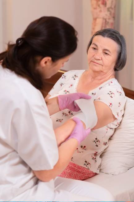 Nurse bandaging elderly woman's arm at home.