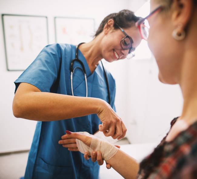 Nurse bandaging patient's hand in clinic.